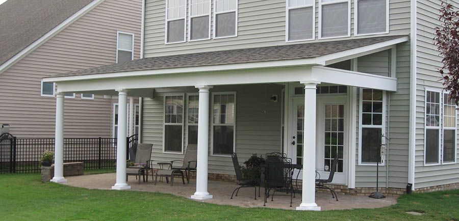 Covered patio with white support columns, shingled roof, and outdoor furniture attached to a two-story house.
