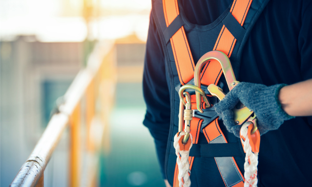 Construction worker wearing a safety harness and clipping a carabiner to a safety rope.