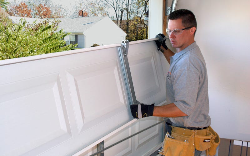 Man in safety gear and a tool belt installing a white sectional garage door.