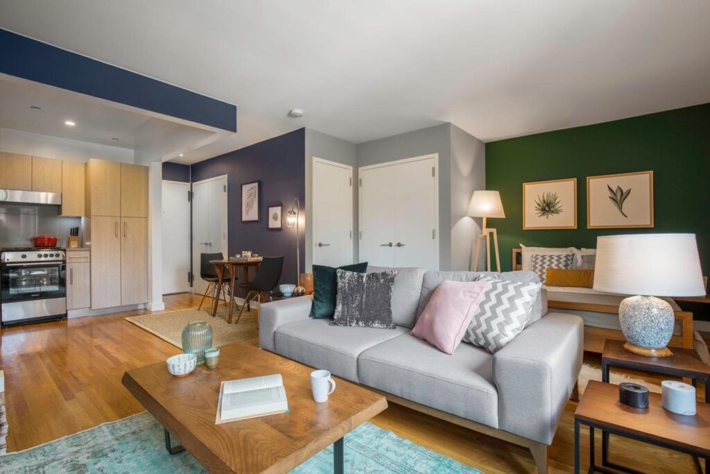 Modern open-concept living room with a grey sofa, wooden coffee table, dining area, and small kitchen.