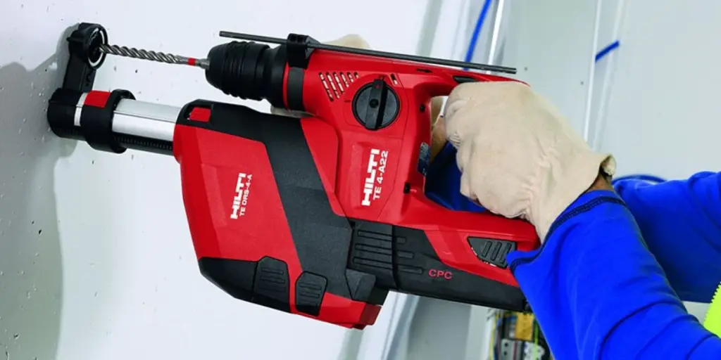 A person in blue clothing and gloves uses a red and black Hilti TE 4-A22 drill to drill into a white wall.