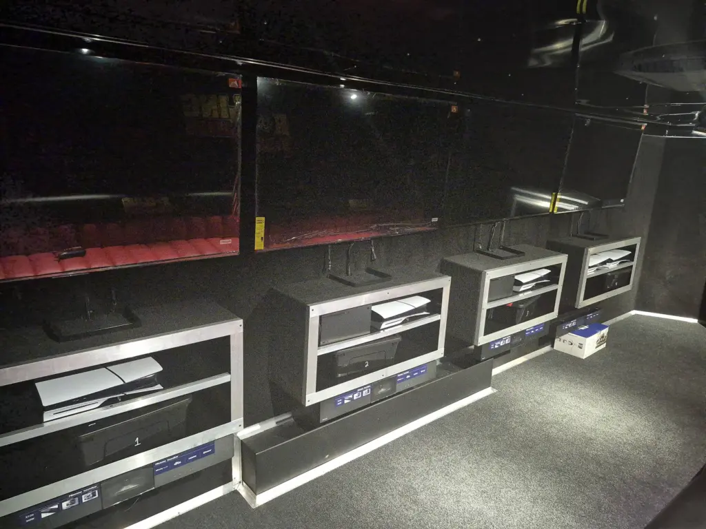 Gaming trailer interior featuring four TV stations, each equipped with a game console and soundbar on a numbered shelf.