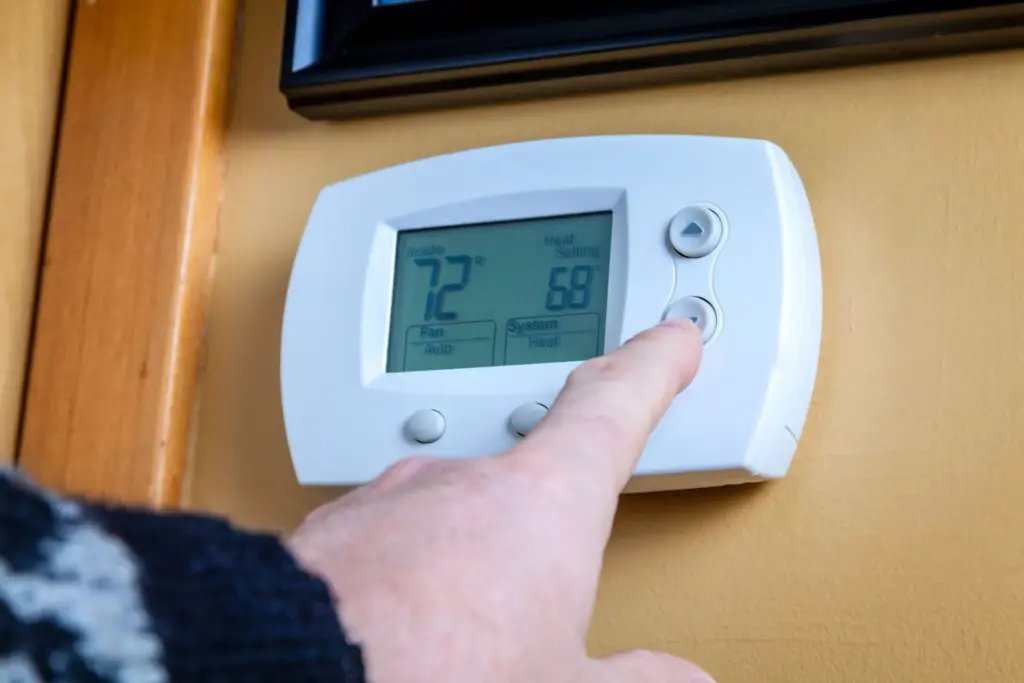 A finger pressing a button on a white digital thermostat.