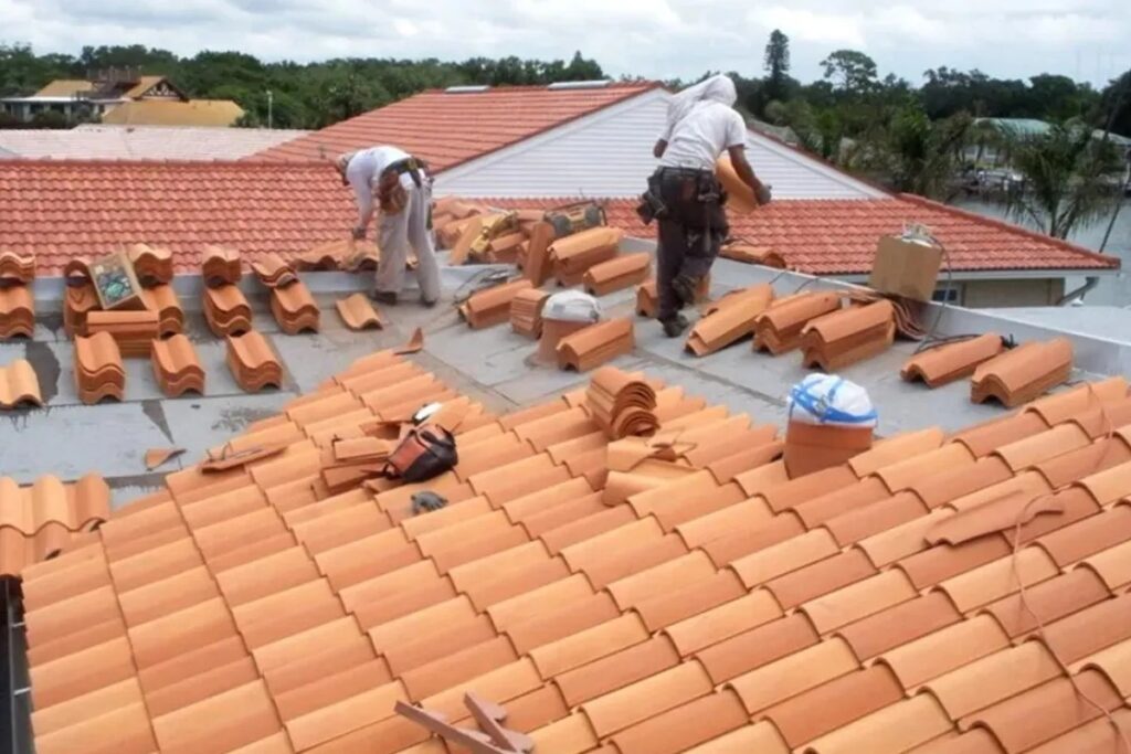 Two roofers installing orange clay tiles on a residential roof.