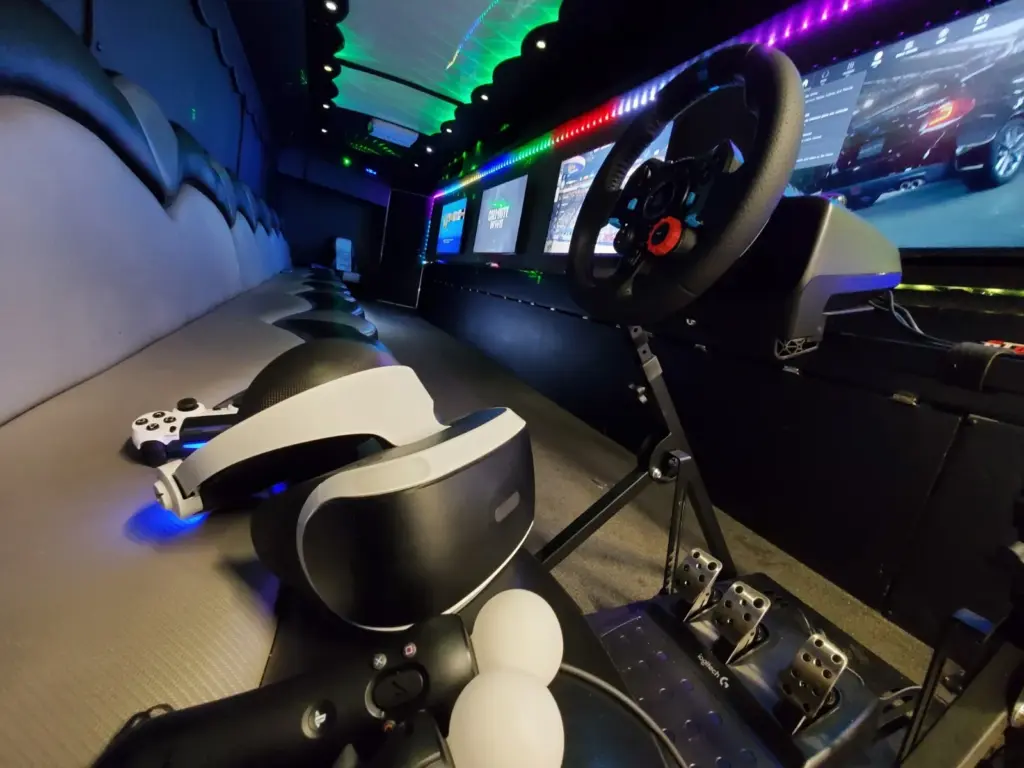 Interior of a gaming van with VR headsets, controllers, and a racing wheel setup on a bench seat.