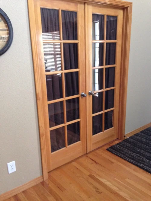 Light-wood French doors with glass panes and dark curtains behind the glass.