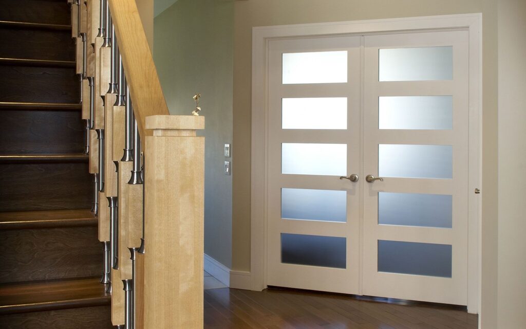 White double doors with frosted glass panels next to a wooden staircase with metal balusters.