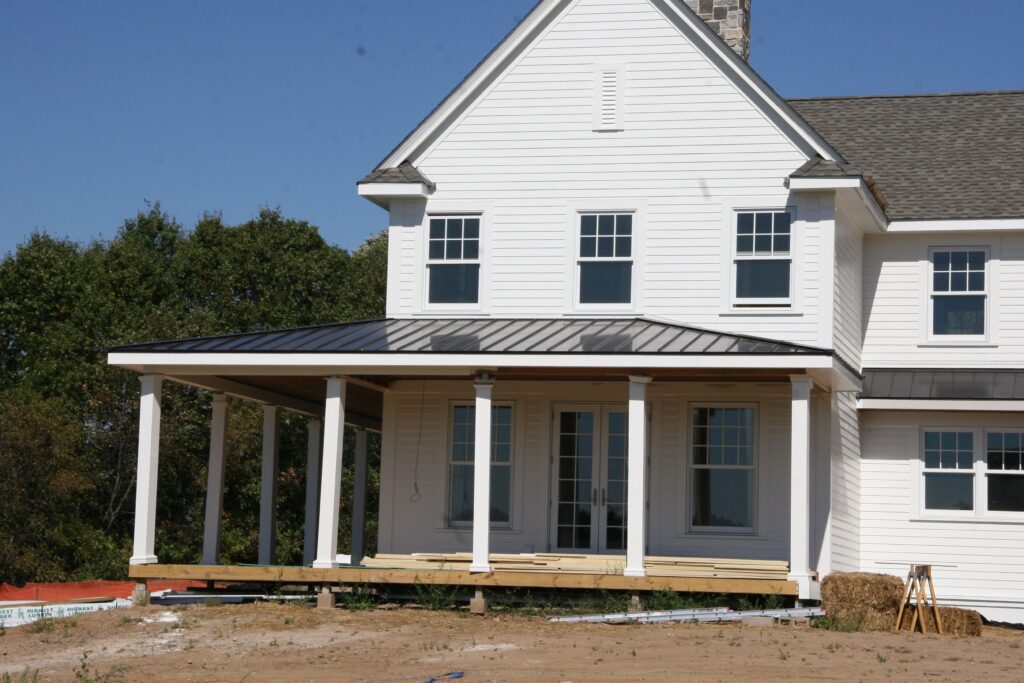 Two-story white house under construction with a dark metal-roofed front porch and white support columns.