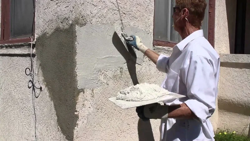 A man applying white plaster to a textured exterior wall using a trowel and hawk.