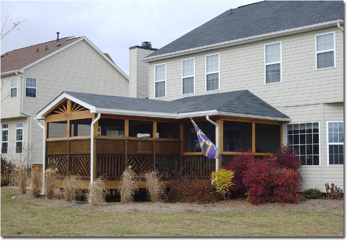 A two-story house featuring an attached wooden screened-in porch with a dark roof and surrounding landscaping.