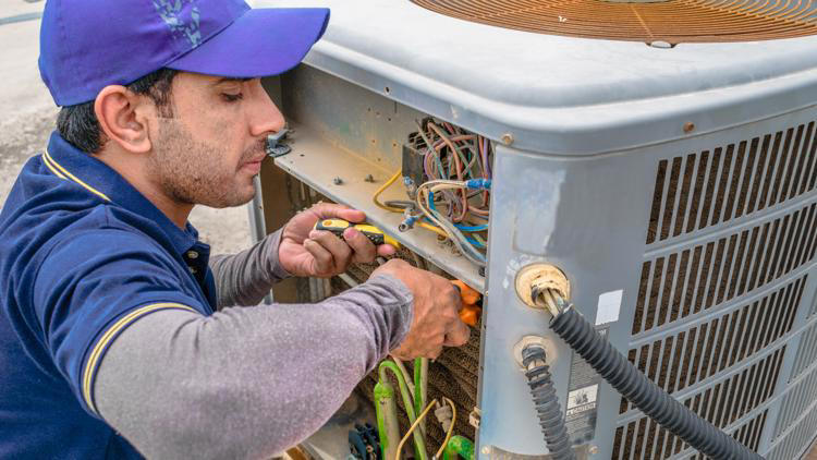 HVAC technician repairing an outdoor air conditioning unit with electrical tools.