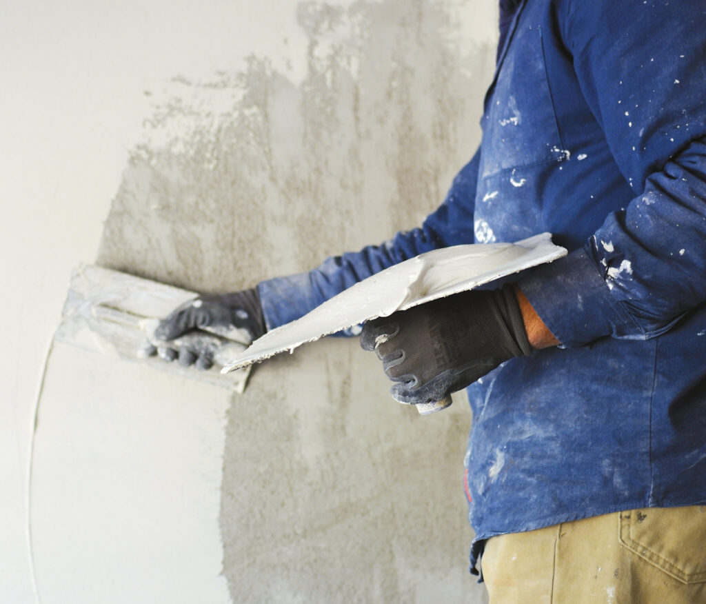 Worker applying plaster to a wall with a trowel and hawk.