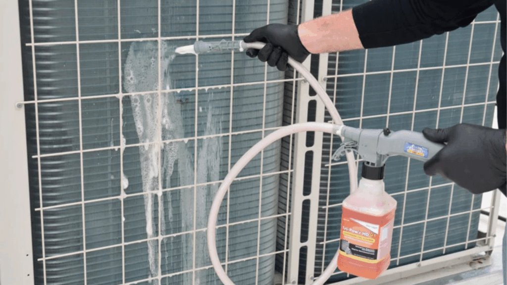 Person in black gloves spraying foam cleaner onto an outdoor air conditioner unit.