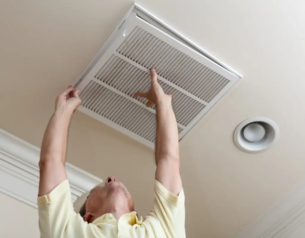 Person removing a white rectangular ceiling vent cover.