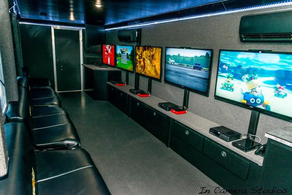 Mobile gaming trailer interior featuring rows of black leather seats facing a wall of multiple large flat-screen TVs.