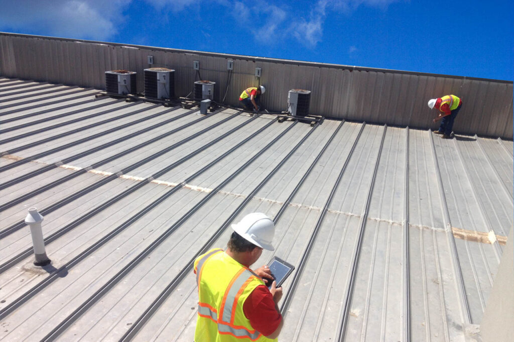 Technicians in high-visibility vests and hard hats working on an industrial metal roof with HVAC units.