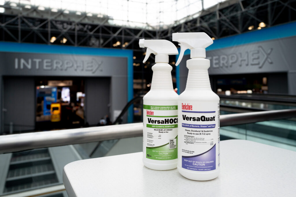 Berkshire VersaHOCl and VersaQuat disinfectant spray bottles with INTERPHEX signage in the background.