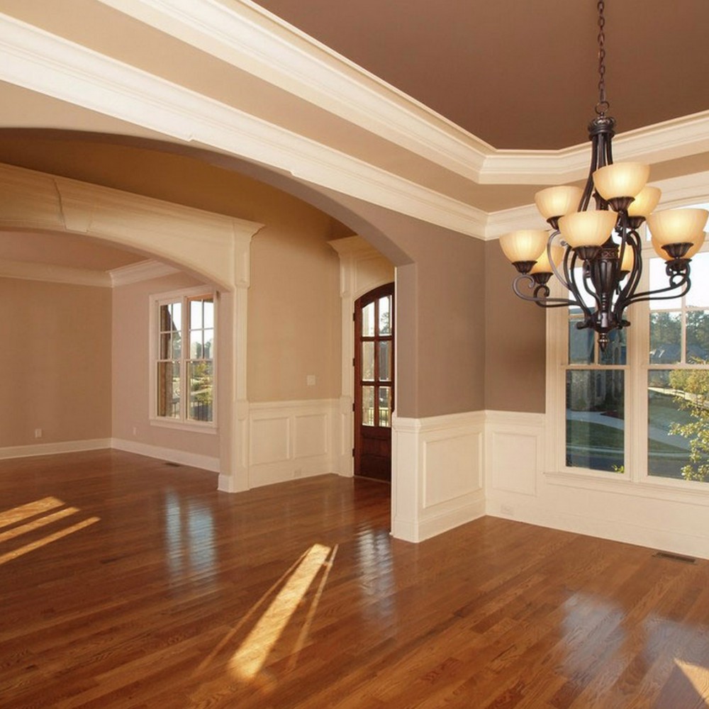 Empty dining room with hardwood floors, white wainscoting, an arched entryway, and a large black chandelier.