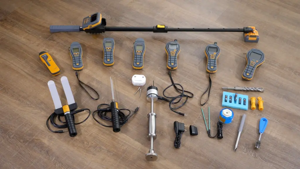 Collection of Protimeter moisture meters, telescopic pole, probes, and testing accessories laid out on a wood floor.