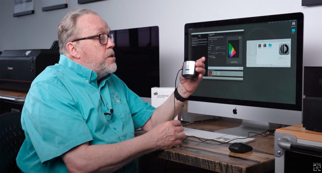 A man demonstrating a color calibration tool for a computer monitor in a workspace.
