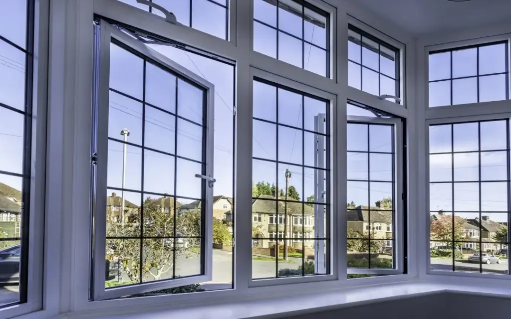 A white bay window unit with open casement windows overlooking a residential suburban street.