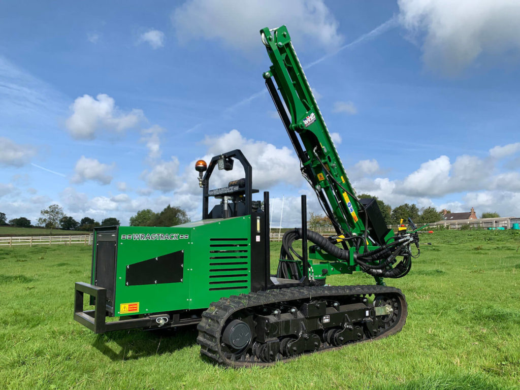 Green Wragtrack tracked drilling rig in a grassy field under a blue sky.