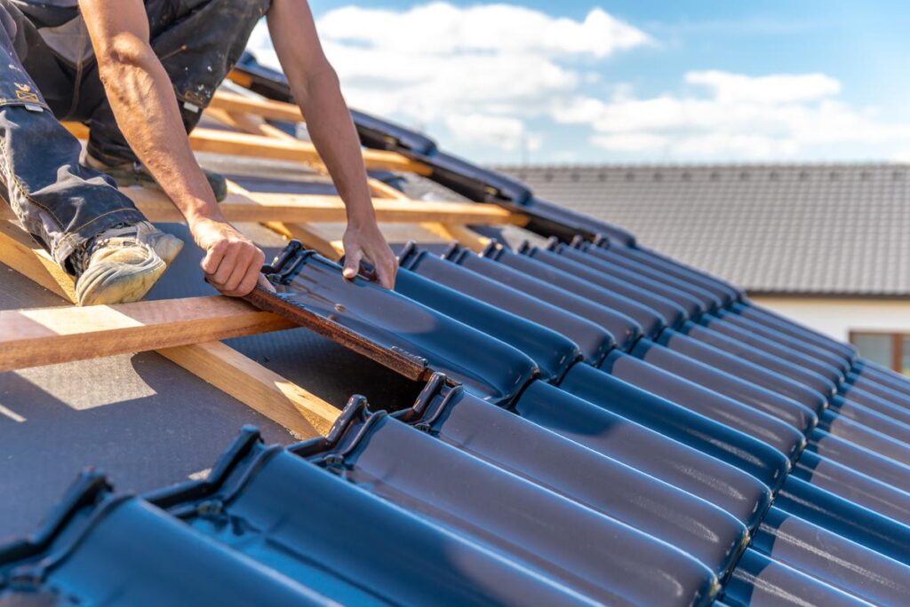 Roofer installing dark blue glazed tiles on a wooden roof frame.
