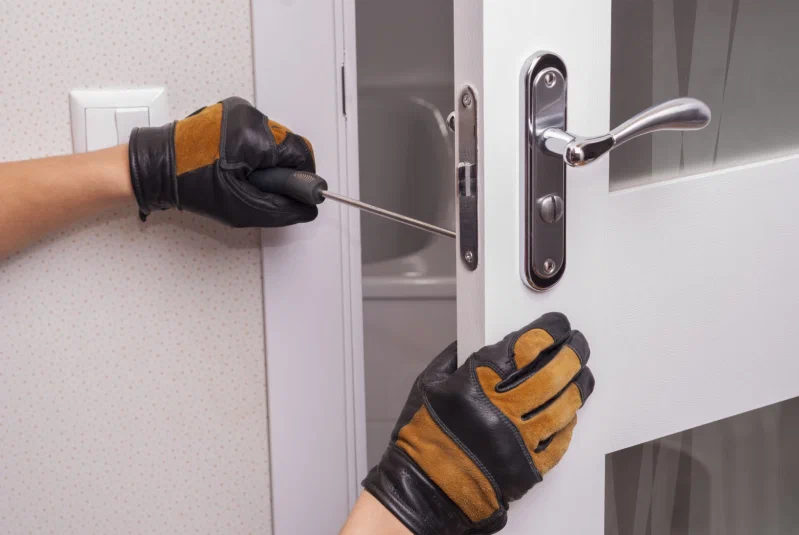 Gloved hands using a screwdriver to adjust white door hardware.
