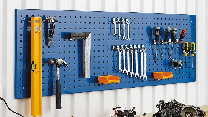Blue pegboard mounted on a white wall holding various tools like a level, hammer, wrenches, and screwdrivers.