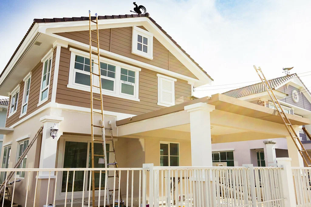 Two-story beige house with white trim and tall wooden ladders propped against the front exterior.
