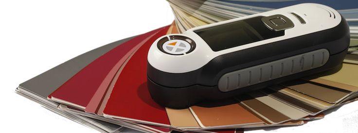 Handheld digital color matching tool resting on fanned-out paint color swatches.