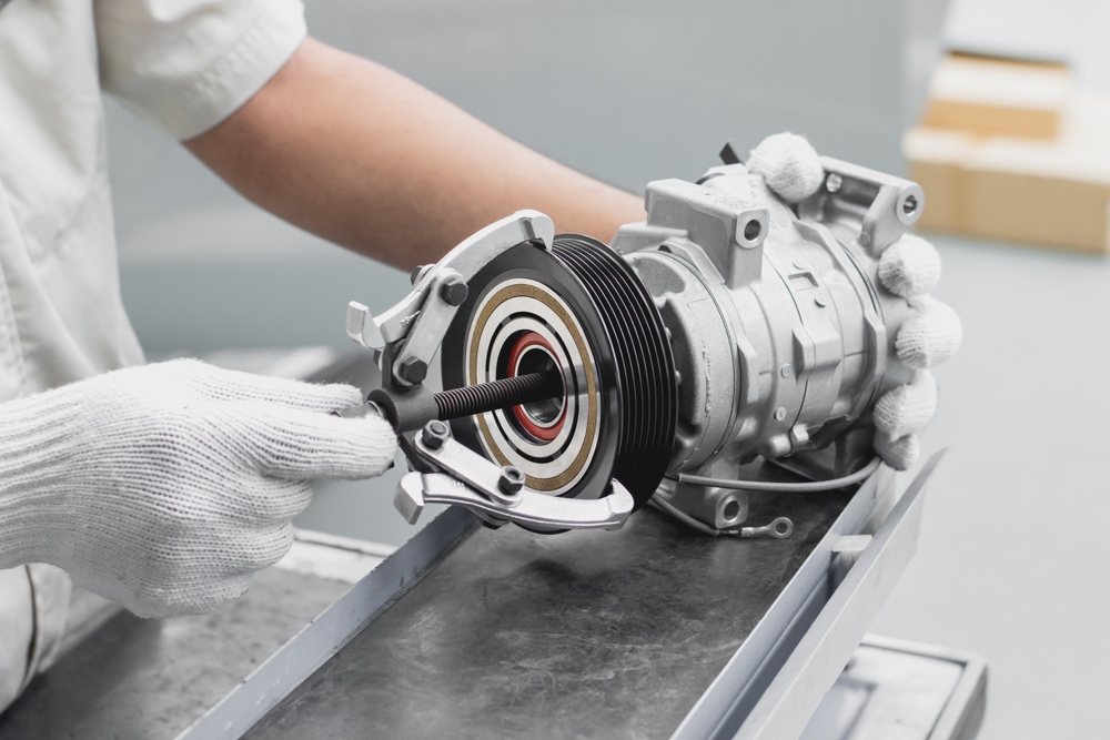Gloved technician using a specialized tool to assemble a metal automotive component.