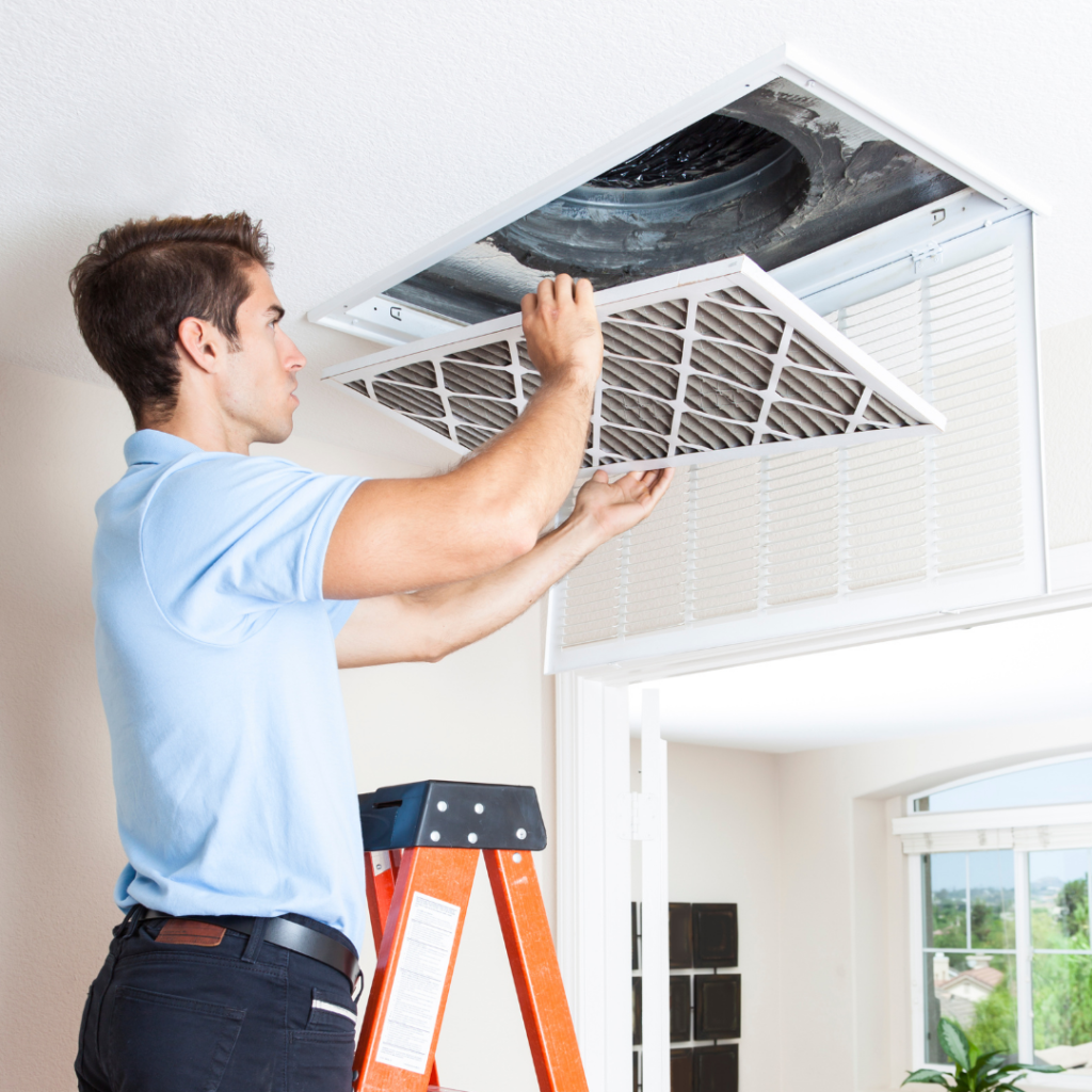 Man on a ladder replacing a ceiling HVAC air filter.