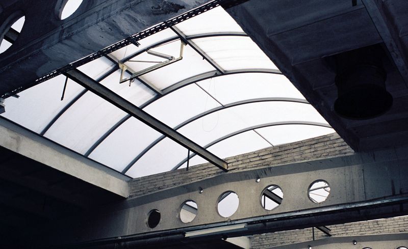 Industrial ceiling featuring curved skylight panels and concrete beams with circular cutouts.
