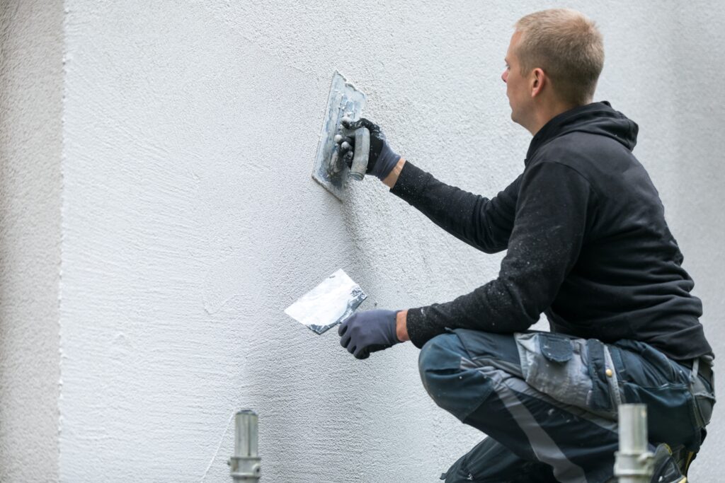 A plasterer using a trowel to smooth white plaster on an exterior wall.