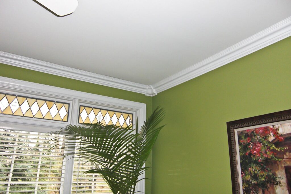 Olive green walls with white crown molding, a palm plant, and a window with decorative stained glass.