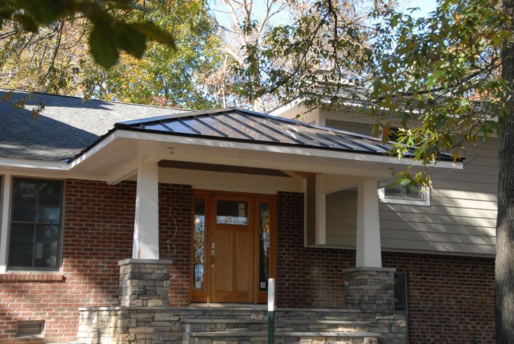 Covered front porch with a dark metal standing seam roof, craftsman stone columns, and a wooden front door.