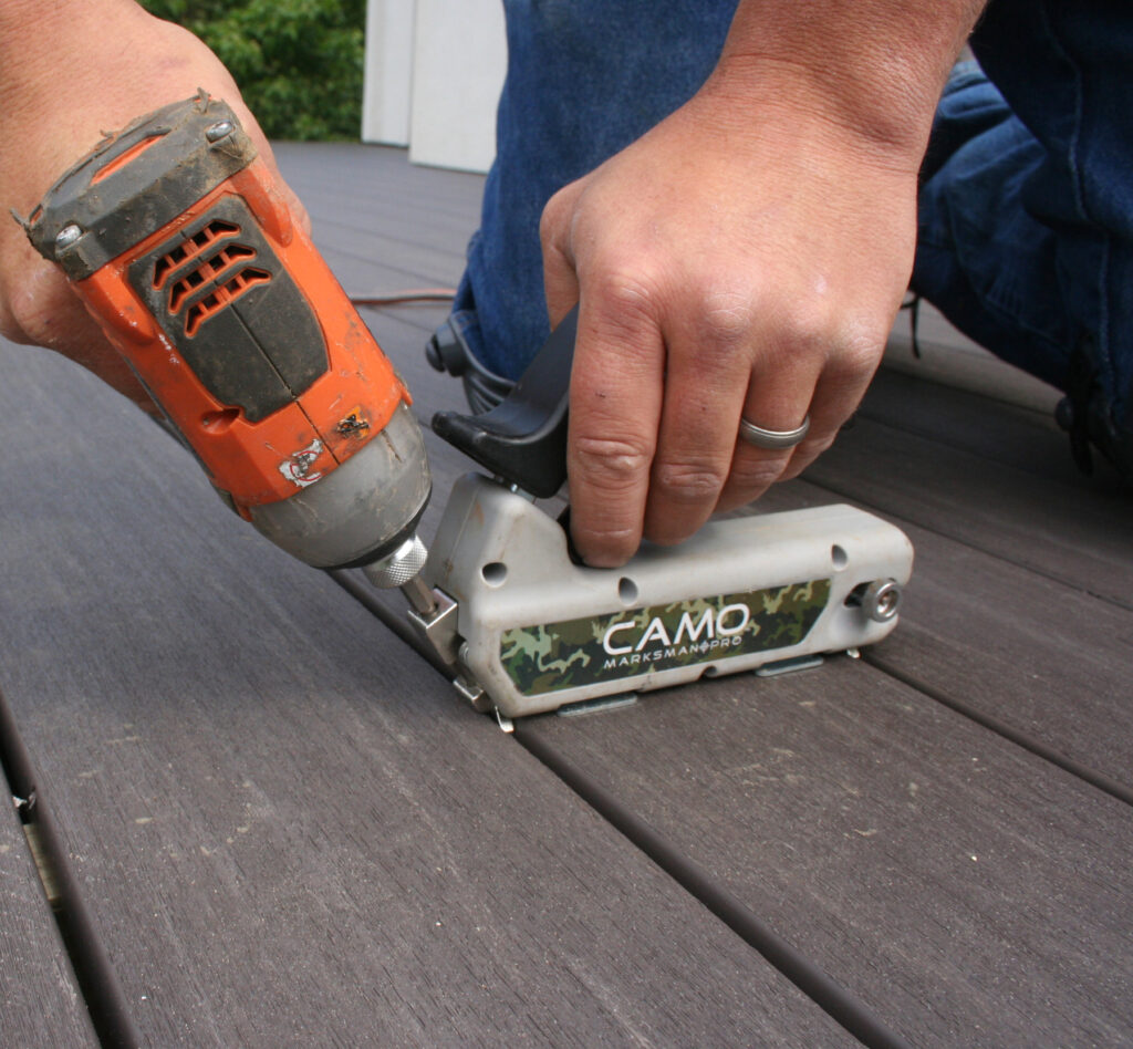 A person uses a power drill and a CAMO Marksman Pro tool to install decking boards.