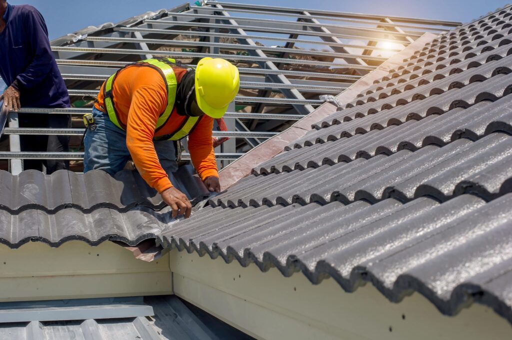 Construction worker in safety gear installing grey roof tiles.