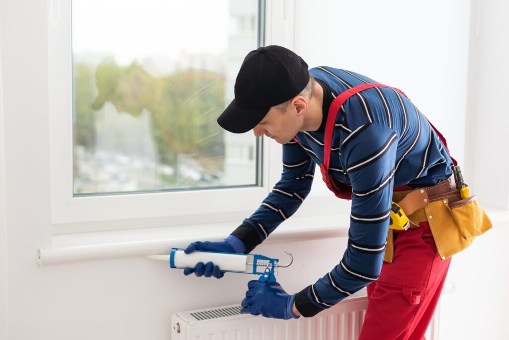 Construction worker in a uniform applying sealant to a window sill with a caulking gun.