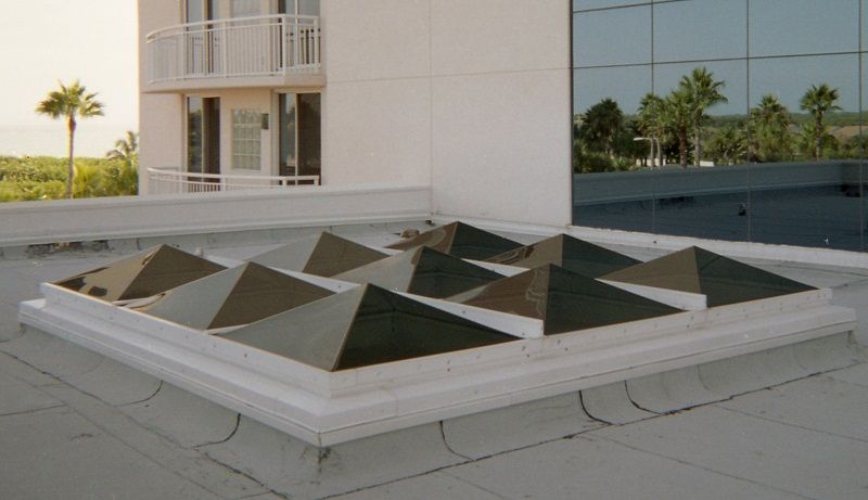 Grid of dark-tinted pyramid skylights on a flat rooftop next to a white building.