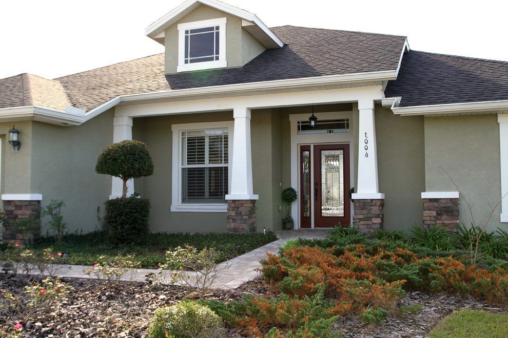 Single-story home with olive green stucco, stone base accents, a dark roof, and a red front door with a glass inlay.
