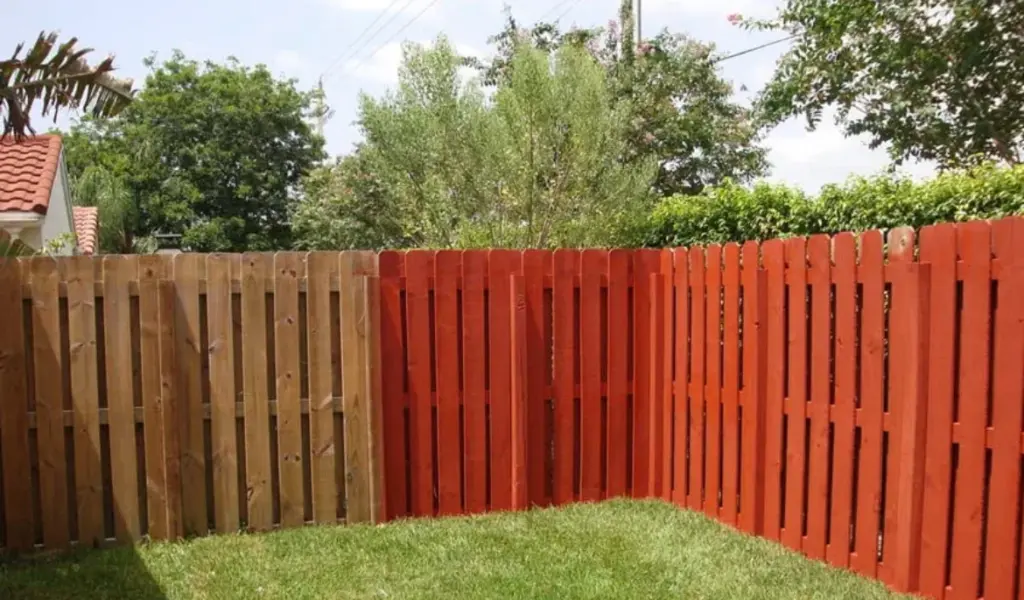 A backyard wooden fence, with one section finished in natural wood and the other painted a bright, solid red.