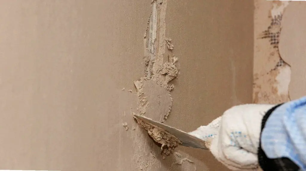 Gloved hand using a putty knife to apply plaster to a wall crack.