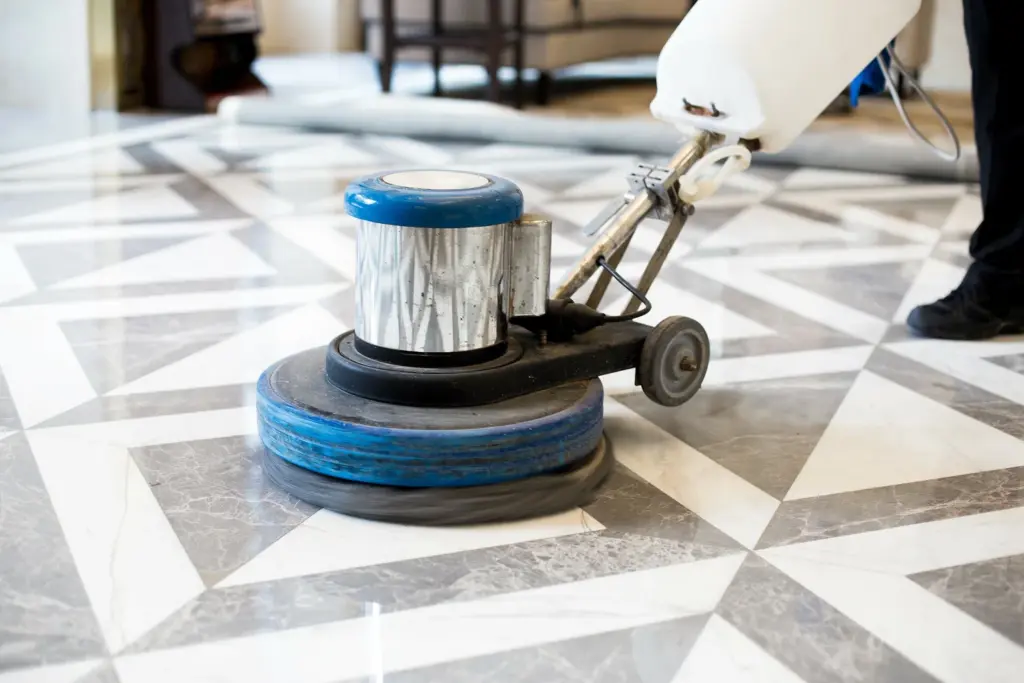 A person using a floor buffer machine on a geometric marble tile floor.