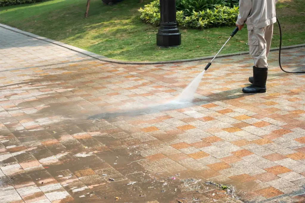 Person using a pressure washer to clean a patterned stone walkway.
