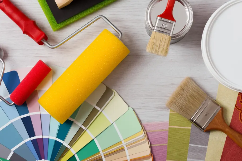 Painting tools, color swatches, and brushes on a white wooden surface.