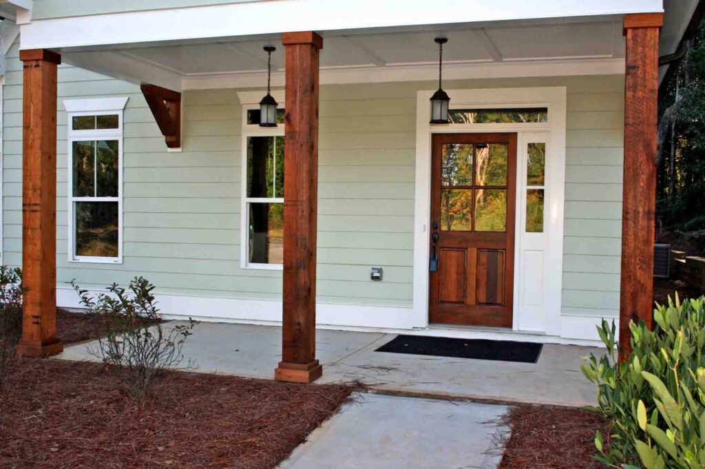 Light green house porch featuring dark wood columns, a wooden door, and hanging lanterns.