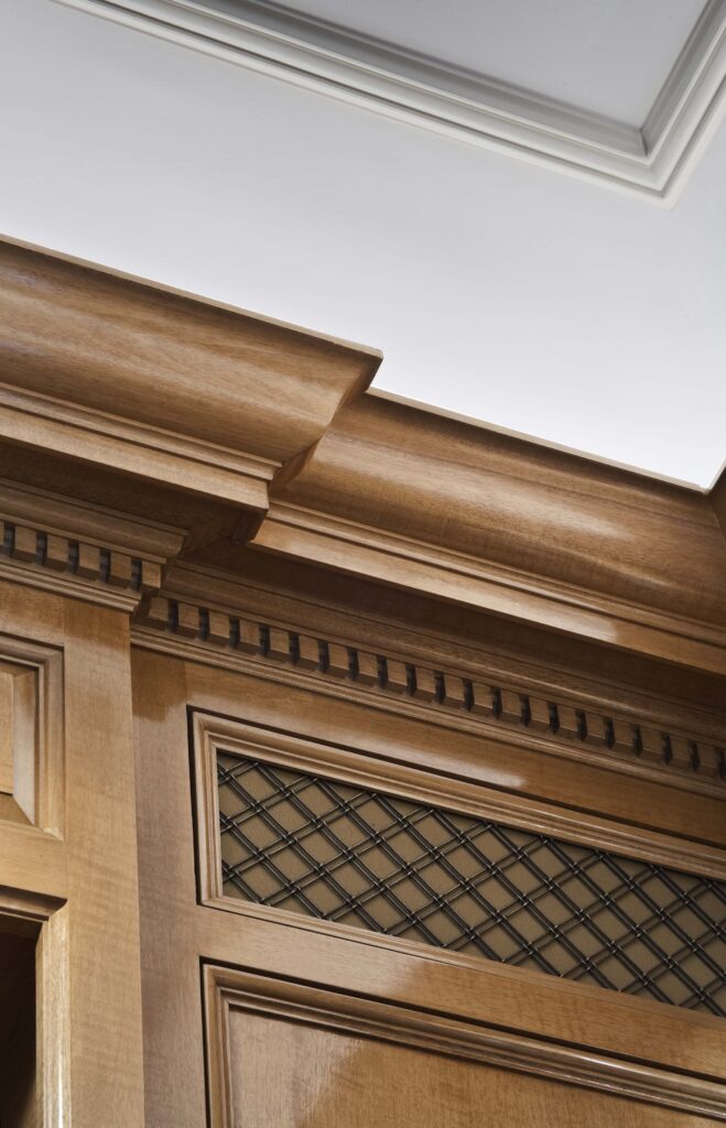 Close-up of polished wood cabinetry featuring crown molding, decorative dentil trim, and a metal lattice insert.