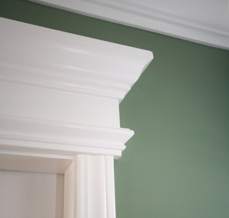 Detail of white architectural molding and crown trim against a sage green wall.